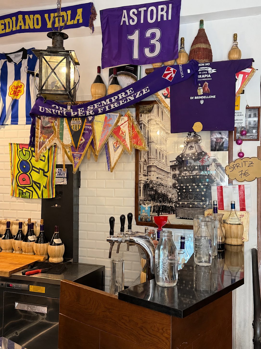 L'interno della Trattoria I' Brindellone: il bancone coi fiaschi impagliati, i gagliardetti viola della Fiorentina e l'omaggio ad Astori 13